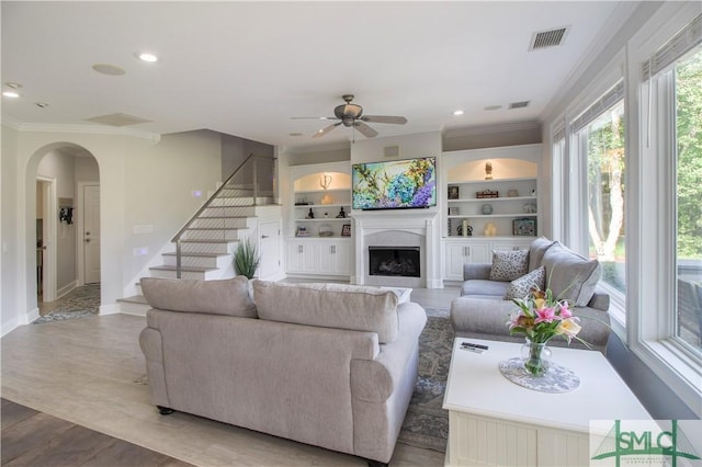 living room featuring visible vents, crown molding, ceiling fan, stairway, and arched walkways