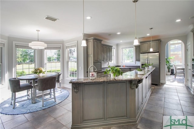 kitchen featuring arched walkways, stone counters, stainless steel fridge, ornamental molding, and recessed lighting