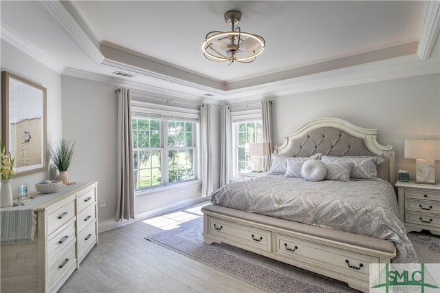 bedroom featuring an inviting chandelier, light wood finished floors, a tray ceiling, visible vents, and ornamental molding