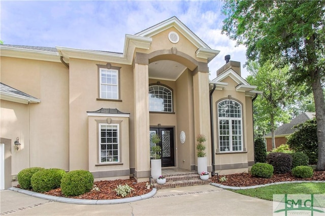 entrance to property featuring a chimney and stucco siding
