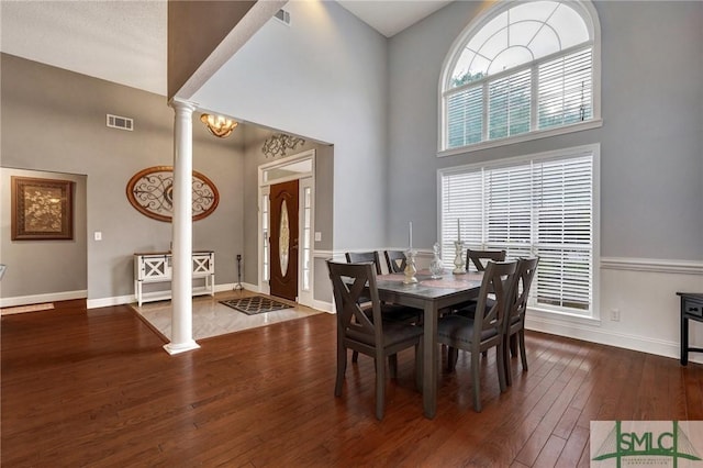 dining space with visible vents, baseboards, wood-type flooring, a high ceiling, and ornate columns