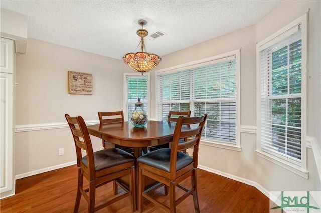 dining space featuring a textured ceiling, baseboards, wood finished floors, and visible vents