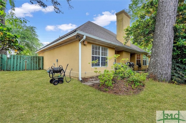 view of side of home featuring a chimney, roof with shingles, a lawn, fence, and stucco siding