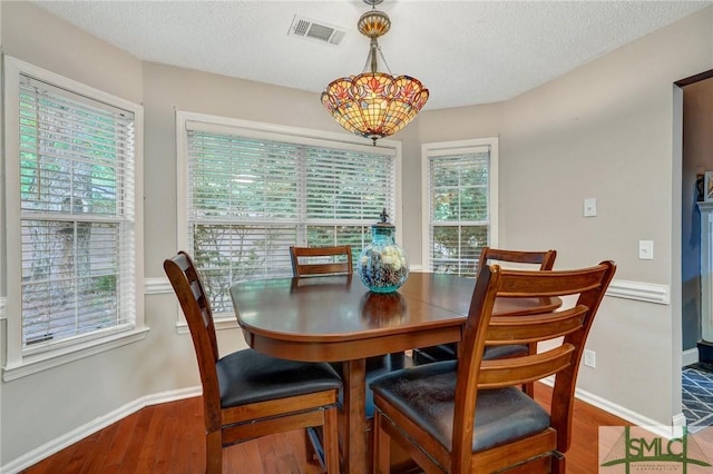 dining room with baseboards, a textured ceiling, wood finished floors, and visible vents
