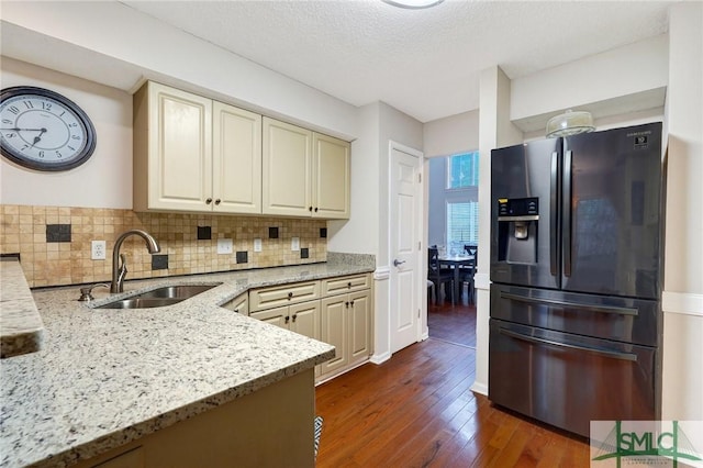 kitchen with light stone countertops, dark wood-style floors, cream cabinets, fridge with ice dispenser, and a sink
