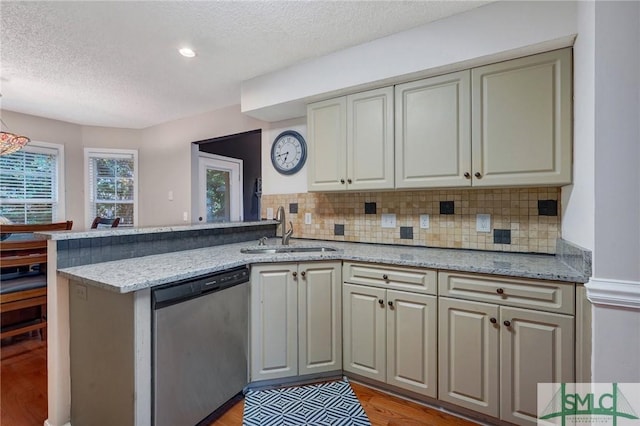 kitchen with stainless steel dishwasher, a peninsula, light wood-type flooring, a textured ceiling, and a sink