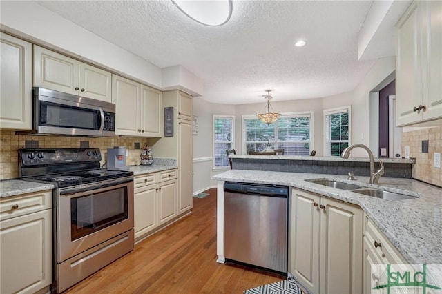 kitchen featuring backsplash, a textured ceiling, appliances with stainless steel finishes, light wood-type flooring, and a sink