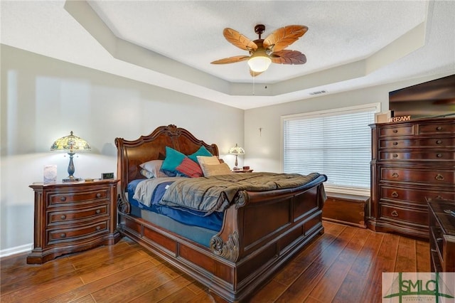 bedroom with ceiling fan, visible vents, dark wood-style floors, and a raised ceiling