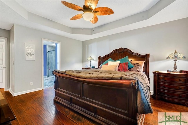 bedroom with baseboards, a raised ceiling, ensuite bath, and hardwood / wood-style flooring