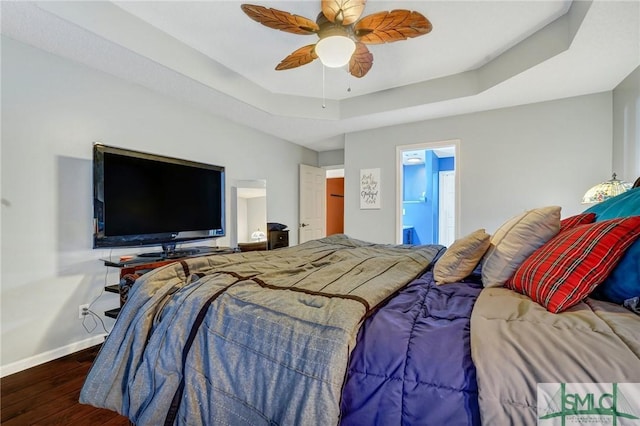 bedroom with a ceiling fan, baseboards, wood finished floors, and a raised ceiling