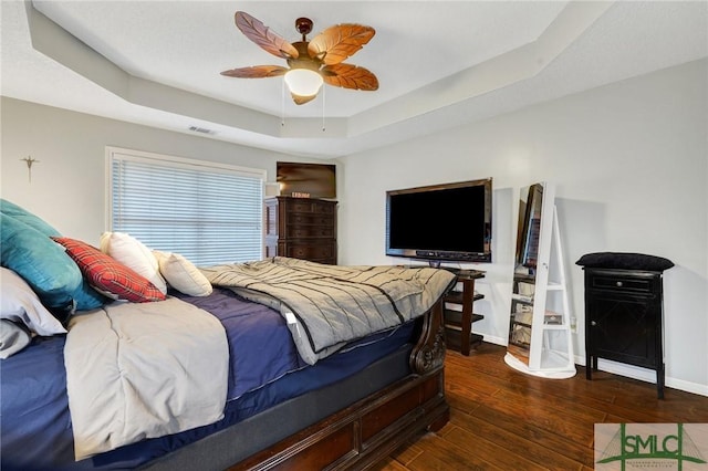 bedroom featuring visible vents, hardwood / wood-style floors, baseboards, a raised ceiling, and a ceiling fan