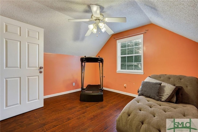 exercise area with ceiling fan, a textured ceiling, baseboards, lofted ceiling, and hardwood / wood-style floors