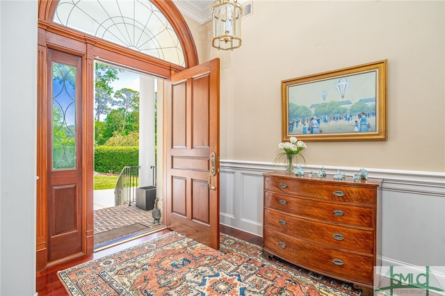 entryway with ornamental molding, a decorative wall, wood finished floors, and a wainscoted wall