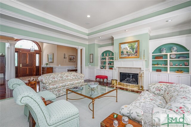 living area featuring ornamental molding, decorative columns, built in features, a wainscoted wall, and a premium fireplace