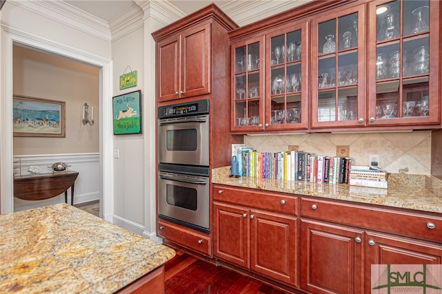 kitchen with double oven, crown molding, light stone countertops, and glass insert cabinets