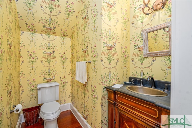 bathroom with vanity, toilet, baseboards, wallpapered walls, and wood finished floors