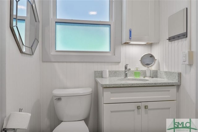 half bath featuring vanity, wood walls, toilet, and a wealth of natural light