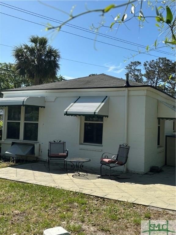 back of house featuring a patio, a shingled roof, and concrete block siding