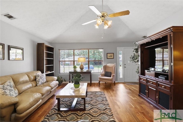 living room with ceiling fan, visible vents, lofted ceiling, and light wood-type flooring
