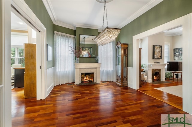 unfurnished living room featuring crown molding, a fireplace with flush hearth, wood finished floors, and a notable chandelier