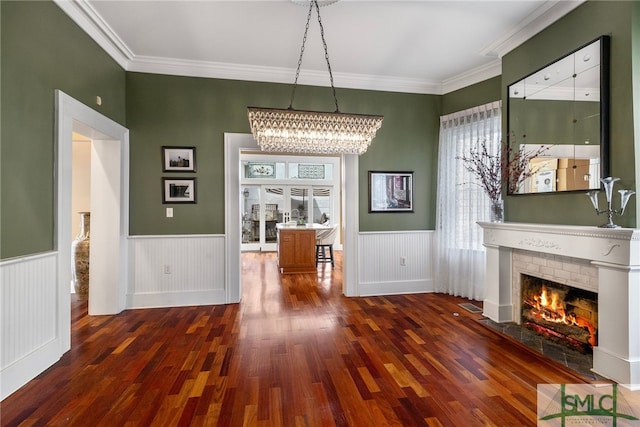 interior space with wood finished floors, a notable chandelier, a fireplace, and a wainscoted wall