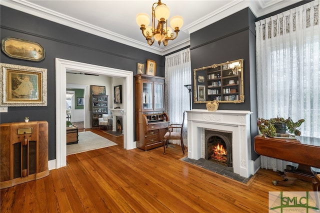 living room featuring wood-type flooring, ornamental molding, baseboards, a fireplace with flush hearth, and a notable chandelier