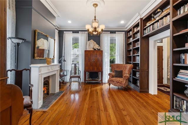 living area featuring an inviting chandelier, ornamental molding, wood-type flooring, and a fireplace with flush hearth