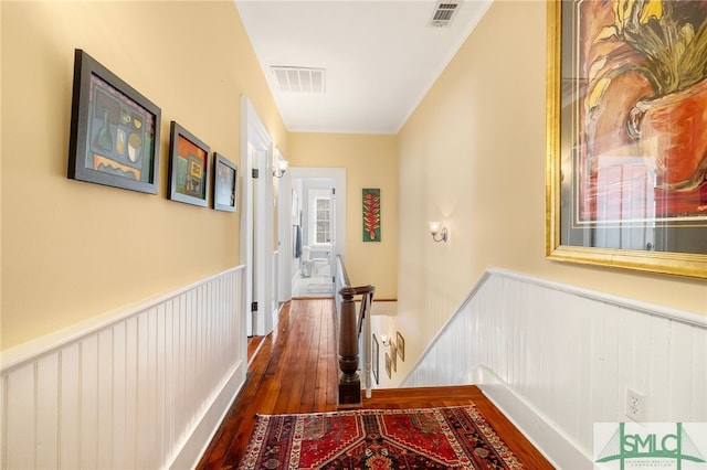 hallway with a wainscoted wall, dark wood-style flooring, and visible vents
