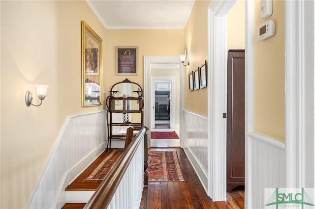 corridor with dark wood-type flooring, ornamental molding, wainscoting, and a decorative wall