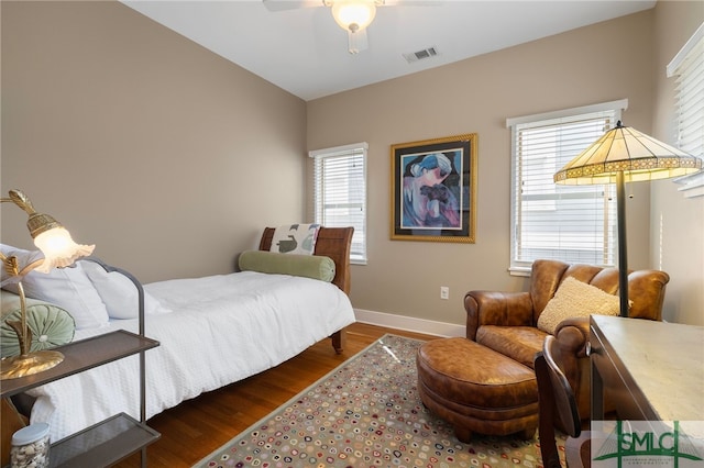 bedroom featuring visible vents, baseboards, wood finished floors, and multiple windows
