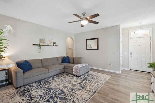 living area with light wood-style floors, arched walkways, baseboards, and ceiling fan