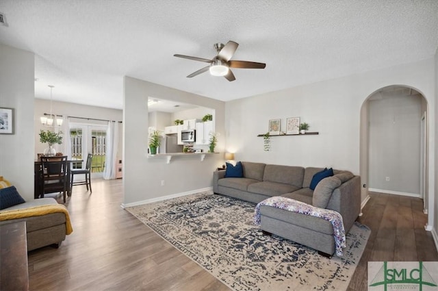 living area featuring ceiling fan, a textured ceiling, arched walkways, wood finished floors, and baseboards