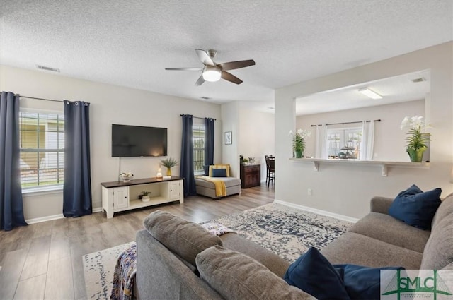 living area featuring a healthy amount of sunlight, a textured ceiling, a ceiling fan, and wood finished floors