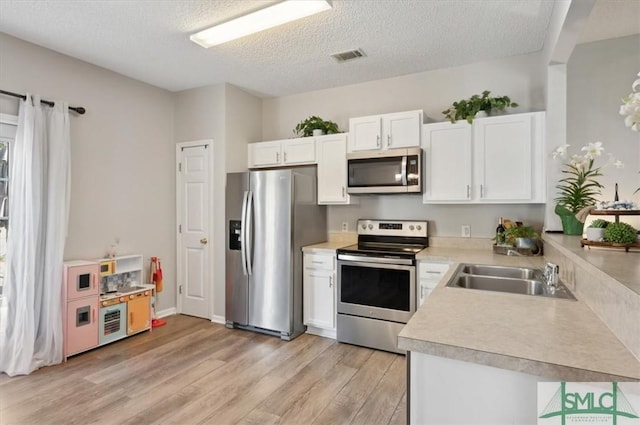 kitchen with a sink, light wood-style floors, light countertops, stainless steel appliances, and white cabinetry