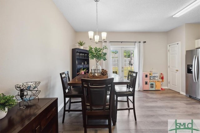 dining area featuring a textured ceiling, a chandelier, french doors, baseboards, and wood finished floors