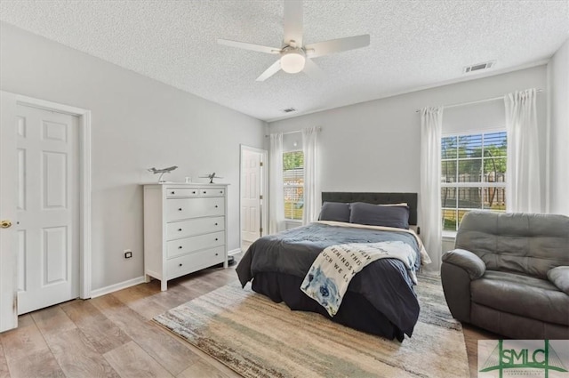 bedroom featuring a ceiling fan, a textured ceiling, visible vents, wood finished floors, and baseboards