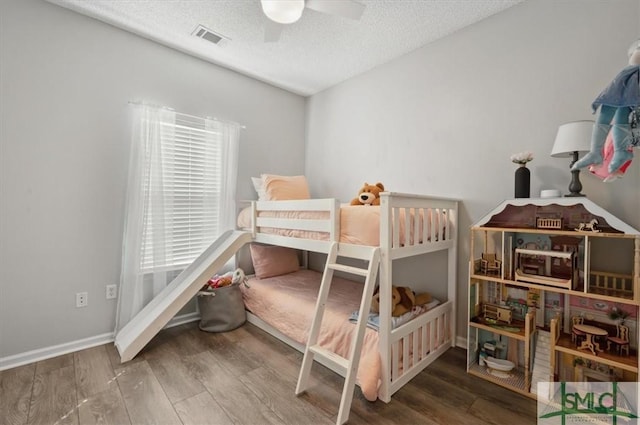 bedroom with ceiling fan, a textured ceiling, visible vents, wood finished floors, and baseboards