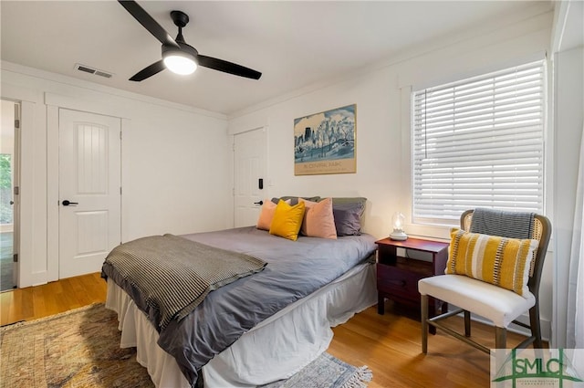 bedroom featuring crown molding, a ceiling fan, visible vents, and wood finished floors