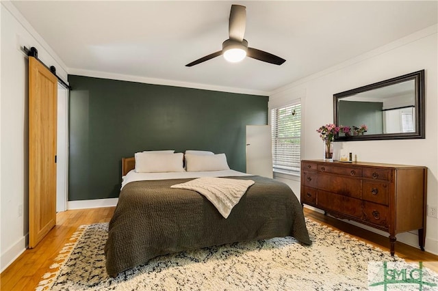 bedroom featuring a barn door, ornamental molding, ceiling fan, and light wood-style floors