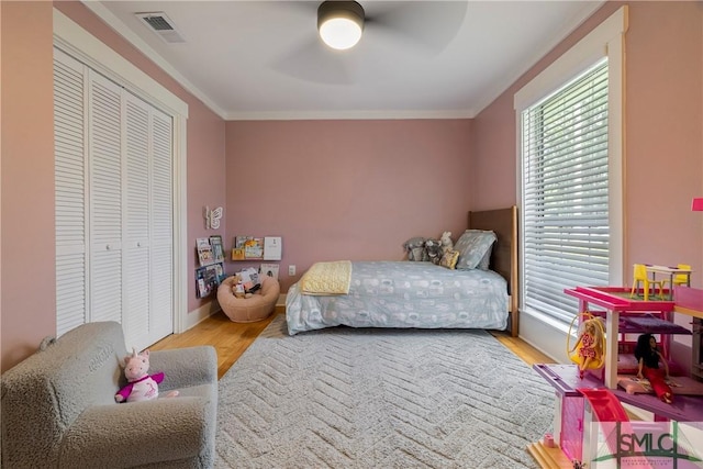 bedroom featuring visible vents, ornamental molding, a closet, wood finished floors, and ceiling fan