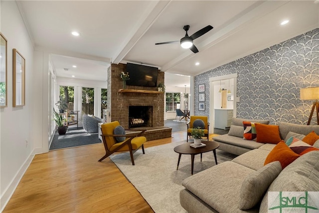 living area featuring a fireplace, beam ceiling, light wood-style floors, an accent wall, and wallpapered walls