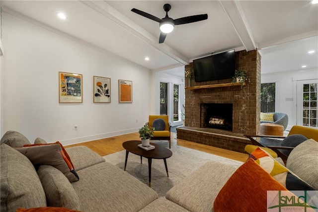 living room featuring ceiling fan, a brick fireplace, baseboards, vaulted ceiling with beams, and wood finished floors