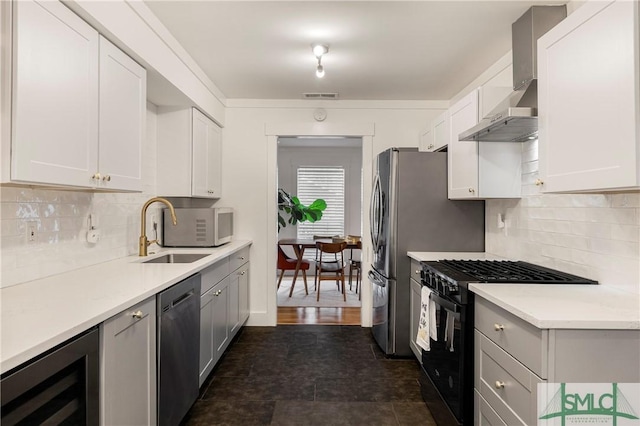 kitchen featuring wall chimney range hood, appliances with stainless steel finishes, light countertops, a sink, and beverage cooler