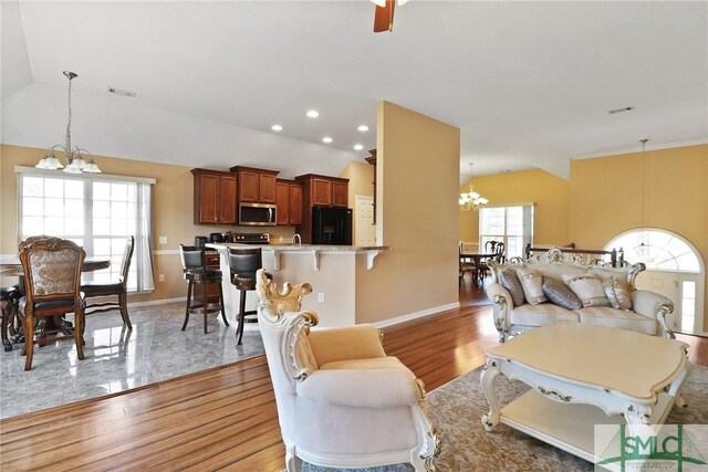 living room featuring visible vents, an inviting chandelier, lofted ceiling, and light wood-type flooring