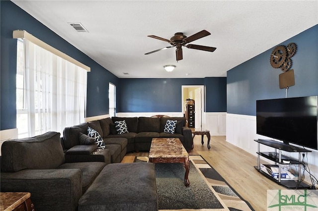 living area featuring a ceiling fan, visible vents, wood finished floors, and a wainscoted wall