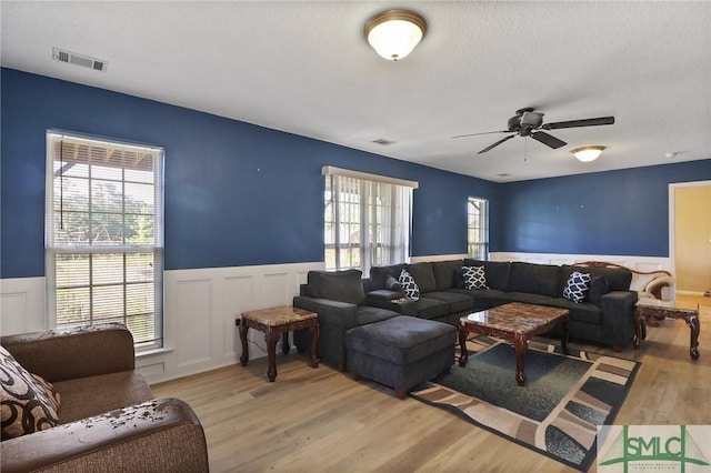 living room featuring visible vents, light wood finished floors, and a wainscoted wall