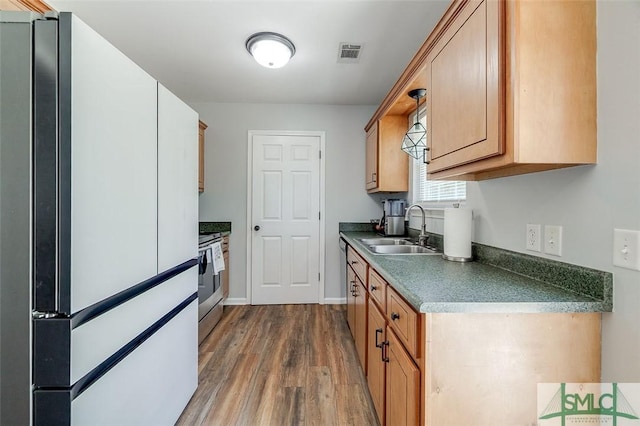 kitchen with visible vents, freestanding refrigerator, wood finished floors, stove, and a sink