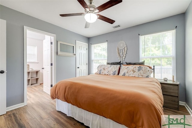 bedroom featuring connected bathroom, a ceiling fan, baseboards, wood finished floors, and visible vents
