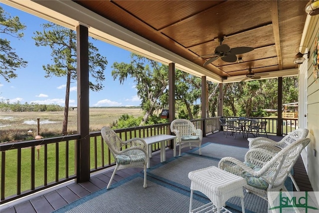 wooden deck with a ceiling fan, a yard, and a rural view