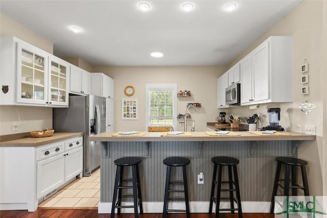 kitchen featuring white cabinets, a peninsula, appliances with stainless steel finishes, and glass insert cabinets